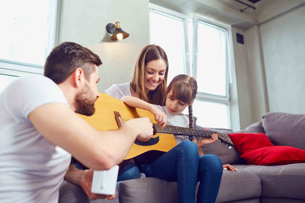 Girl getting guitar tips from mom and dad